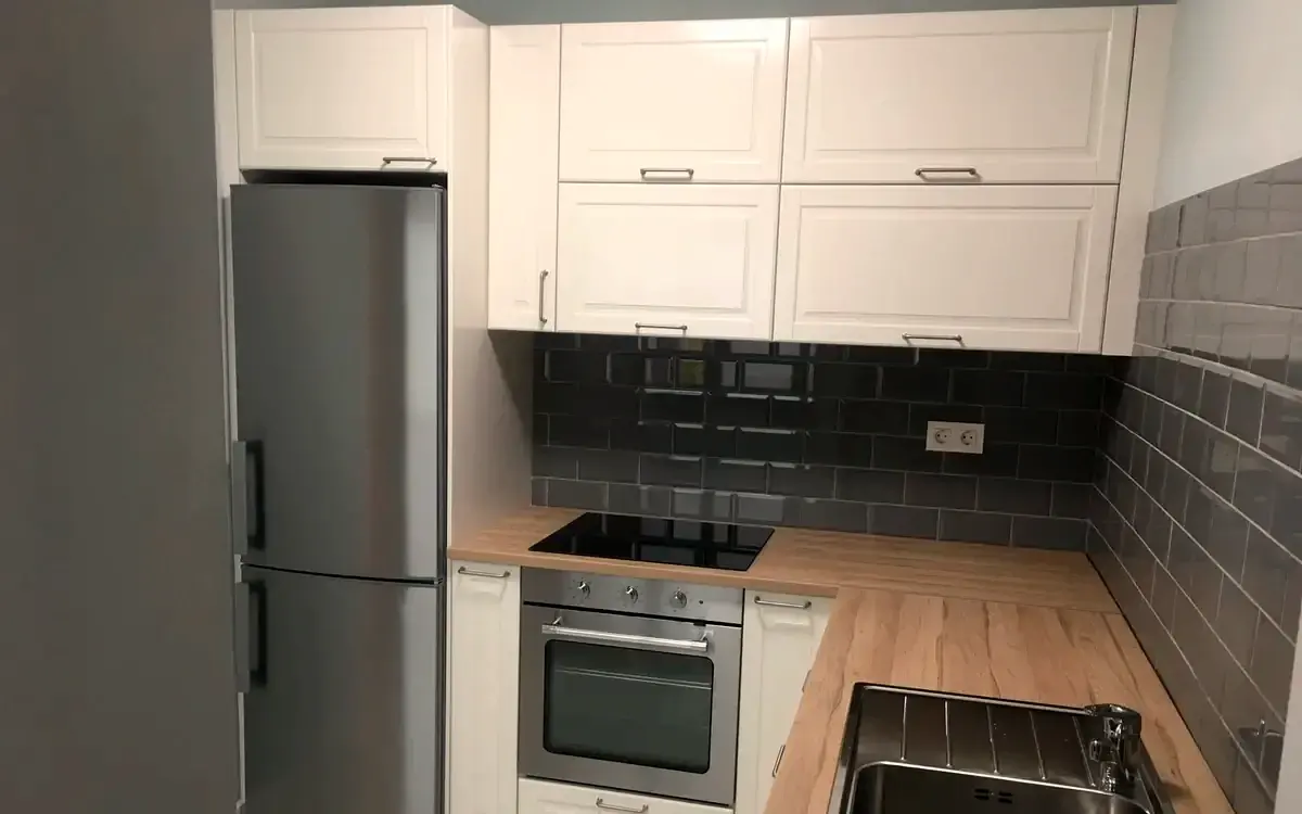 Cocina terminada con muebles blancos, encimera de madera y alicatado gris